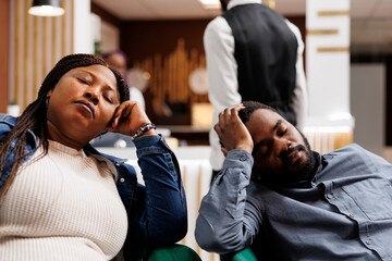 Young tired African American couple napping in hotel lobby, arriving too early at resort, resting...