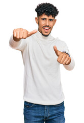 Young arab man wearing casual winter sweater approving doing positive gesture with hand, thumbs up smiling and happy for success. winner gesture.