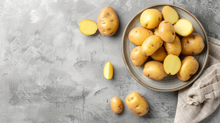 Plate with cut and whole raw potatoes on light background
