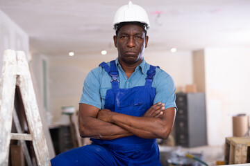 Portrait of confident african-american worker in blue overalls in a room being renovated