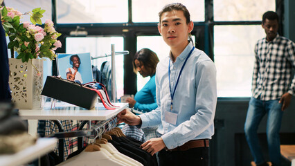 Asian worker arranging new fashion collection, putting hangers with fashionable merchandise on...