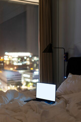 Laptop with empty display on bed and window with city view in cozy hotel room