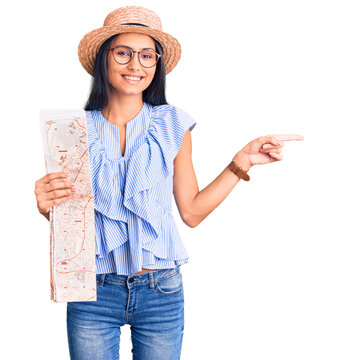 Young beautiful latin girl wearing summer hat holding map smiling happy pointing with hand and finger to the side