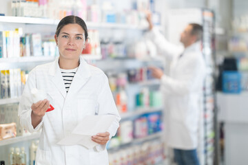 Young female pharmacist in uniform looking for prescription medicine in pharmacy