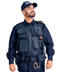 Young hispanic man wearing police uniform looking away to side with smile on face, natural...