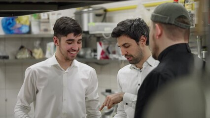 Waiters in white shirts communicate with a professional chef in a black shirt about a specific dish in the kitchen in a restaurant