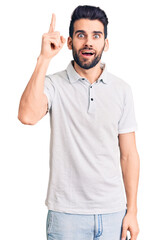 Young handsome man with beard wearing casual polo pointing finger up with successful idea. exited and happy. number one.