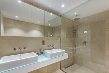The hotel's bathroom is decorated with beige tiles, with a shower cabin and a large mirror.