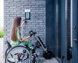 A woman in a wheelchair with an assistive device for manual control enters the entrance. Electric...