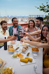 Vertical. Gathering cheerful young multiracial friends toasting red wine celebrating rooftop party....