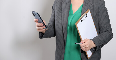 Close up of a young business woman holding a white paper clipboard and a smart phone