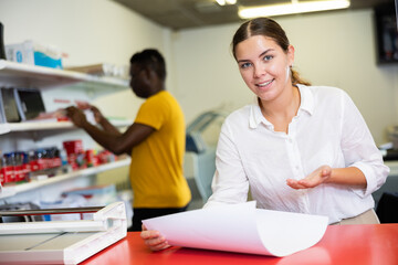 Obraz premium Attentive young female specialist verifying printed sheet during work in the print shop