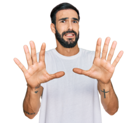 Young hispanic man wearing casual white t shirt afraid and terrified with fear expression stop gesture with hands, shouting in shock. panic concept.