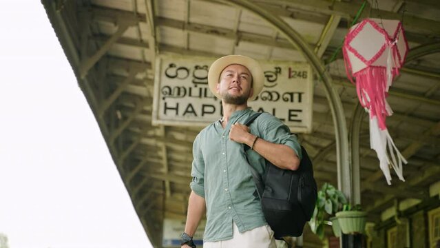 Asian travel blogger at Haputale station captures surroundings. Man with camera and backpack explores scenic train stop, experiences local culture. Adventurer documents journey in Sri Lanka. Slowmo