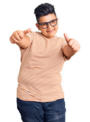 Little boy kid wearing casual clothes and glasses approving doing positive gesture with hand, thumbs up smiling and happy for success. winner gesture.