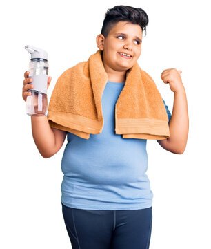 Little boy kid wearing sportswear drinking bottle of water pointing thumb up to the side smiling happy with open mouth