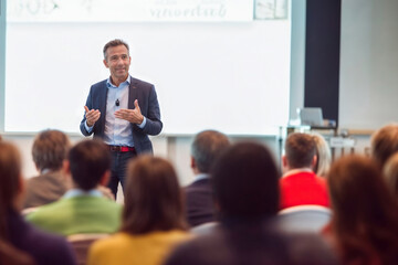 A man stands confidently in front of a diverse crowd of people, possibly delivering a speech or presentation.