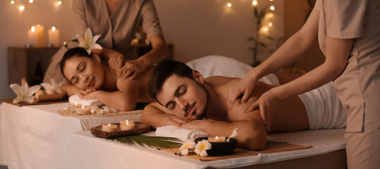 Young couple getting massage from therapists in dark spa salon