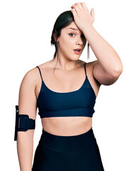 Young hispanic woman wearing sportswear surprised with hand on head for mistake, remember error....