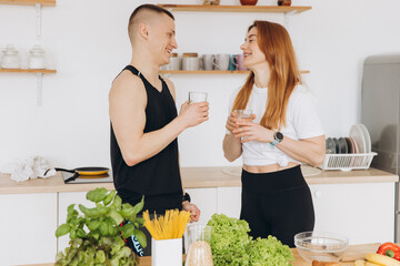 Happy smiling couple of athletes drinking clean water and cooking healthy food in the kitchen at...