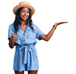 Young indian girl wearing summer hat showing palm hand and doing ok gesture with thumbs up, smiling happy and cheerful