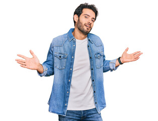Young hispanic man wearing casual clothes clueless and confused expression with arms and hands...
