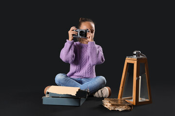Cute little girl with photo camera and typewriter on dark background