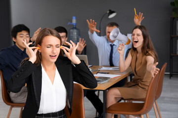 Young businesswoman with earplugs suffering from noisy colleagues in office