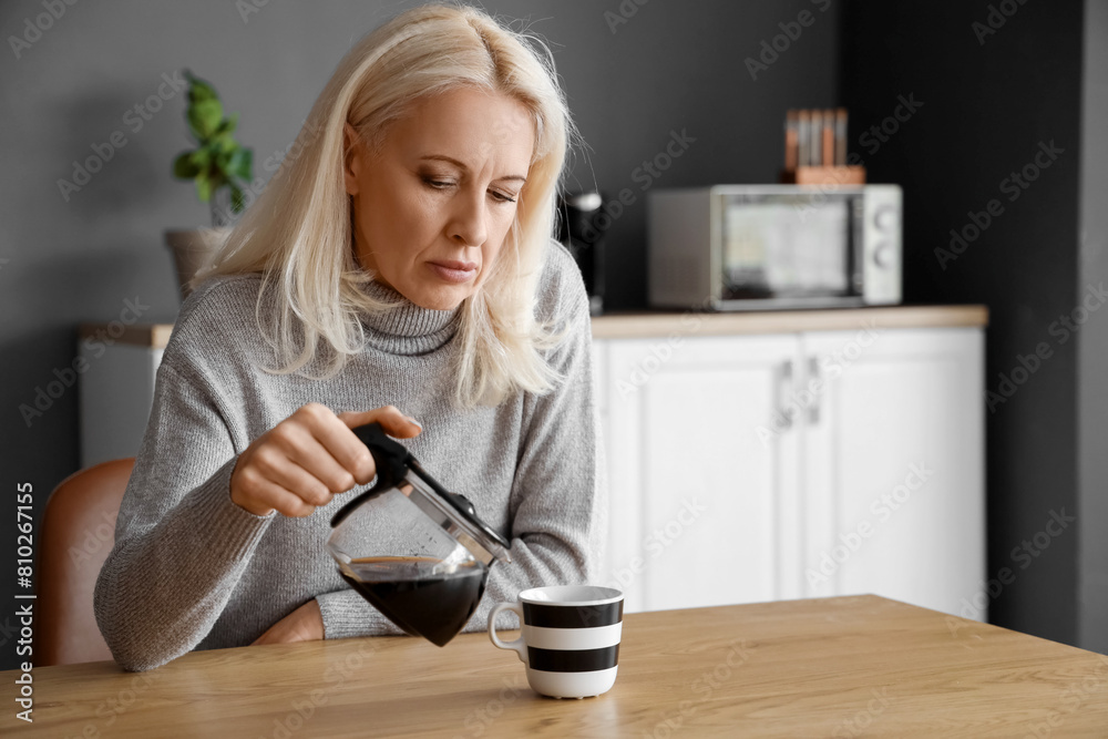 Wall mural Depressed mature woman pouring coffee in kitchen