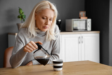 Depressed mature woman pouring coffee in kitchen