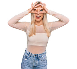 Young blonde woman wearing casual clothes doing ok gesture like binoculars sticking tongue out, eyes looking through fingers. crazy expression.