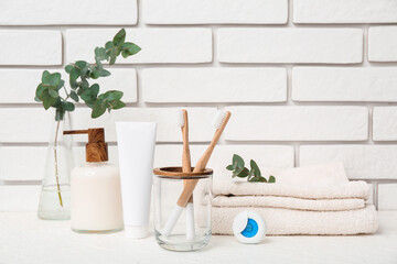 Set of bath supplies with eucalyptus branches on table against light brick wall