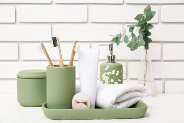 Set of bath supplies and vase with eucalyptus branches on table near light brick wall
