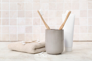 Set of bath supplies with bamboo toothbrushes on table against light tile wall - obrazy, fototapety, plakaty