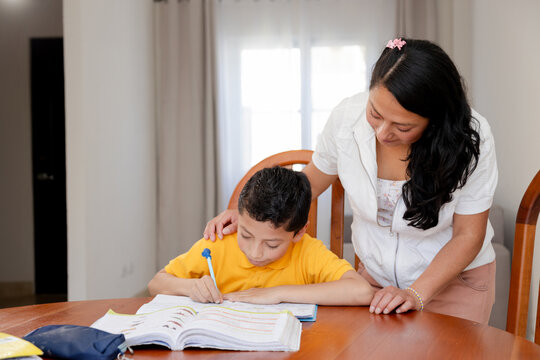 Hispanic mom helping her son do homework-mom and son studying at home-teacher with her student-homeschooling