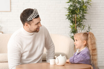 Happy father with his cute little daughter in princess crowns having tea party at home