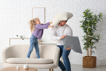 Emotional father with his cute little daughter fighting pillows at home