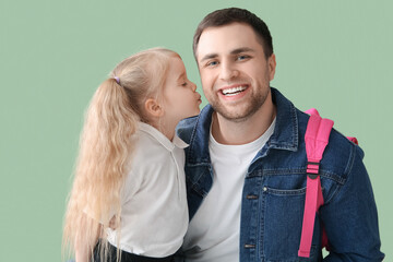 Cute little schoolgirl kissing her happy father on green background