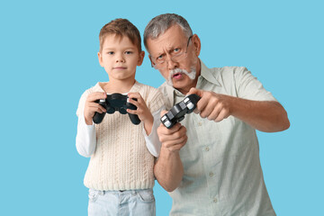 Grandfather with his cute little grandson playing video games on blue background
