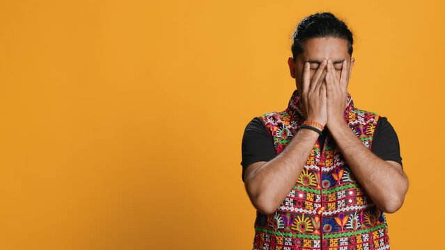 Anxious indian man covering face with palms, worried about future, isolated over studio background. Tense person massaging temples, bothered by troubling news, feeling distressed, camera A