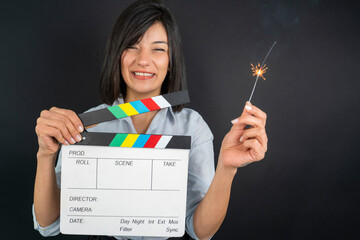 A happy young woman holding a movie clapboard and a lit sparkler.