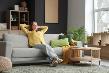 Young woman resting on grey sofa in living room