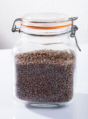 Glass bottle of dry lentils on white background