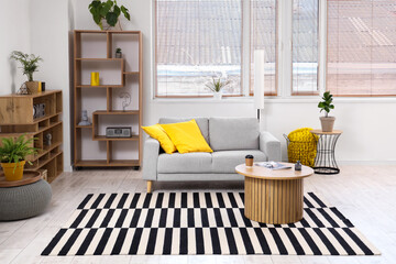 Modern interior of light living room with cozy sofa, shelving units, houseplants and coffee table