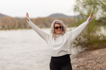 Happy mature woman raising hands by the river