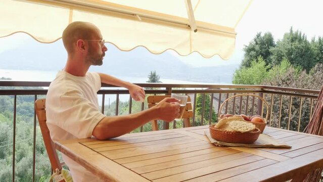 young man 30-35 years old drinks tea from glass cup and eats rice cookies, tea drinking on balcony, loggia flooded with warm light, relaxation in Italy