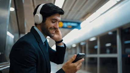 Smart business man listening music by headphone while waiting train at train station with blurring...