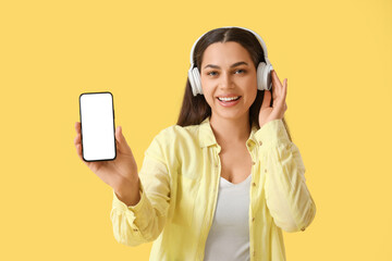 Beautiful young happy woman in headphones listening music on yellow background