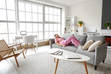 Beautiful young happy woman in headphones listening music and lying on sofa at home