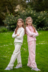 Fototapeta premium Two friendly girls in light-toned clothing with smiles enjoying a spring day in the park, standing on green grass.